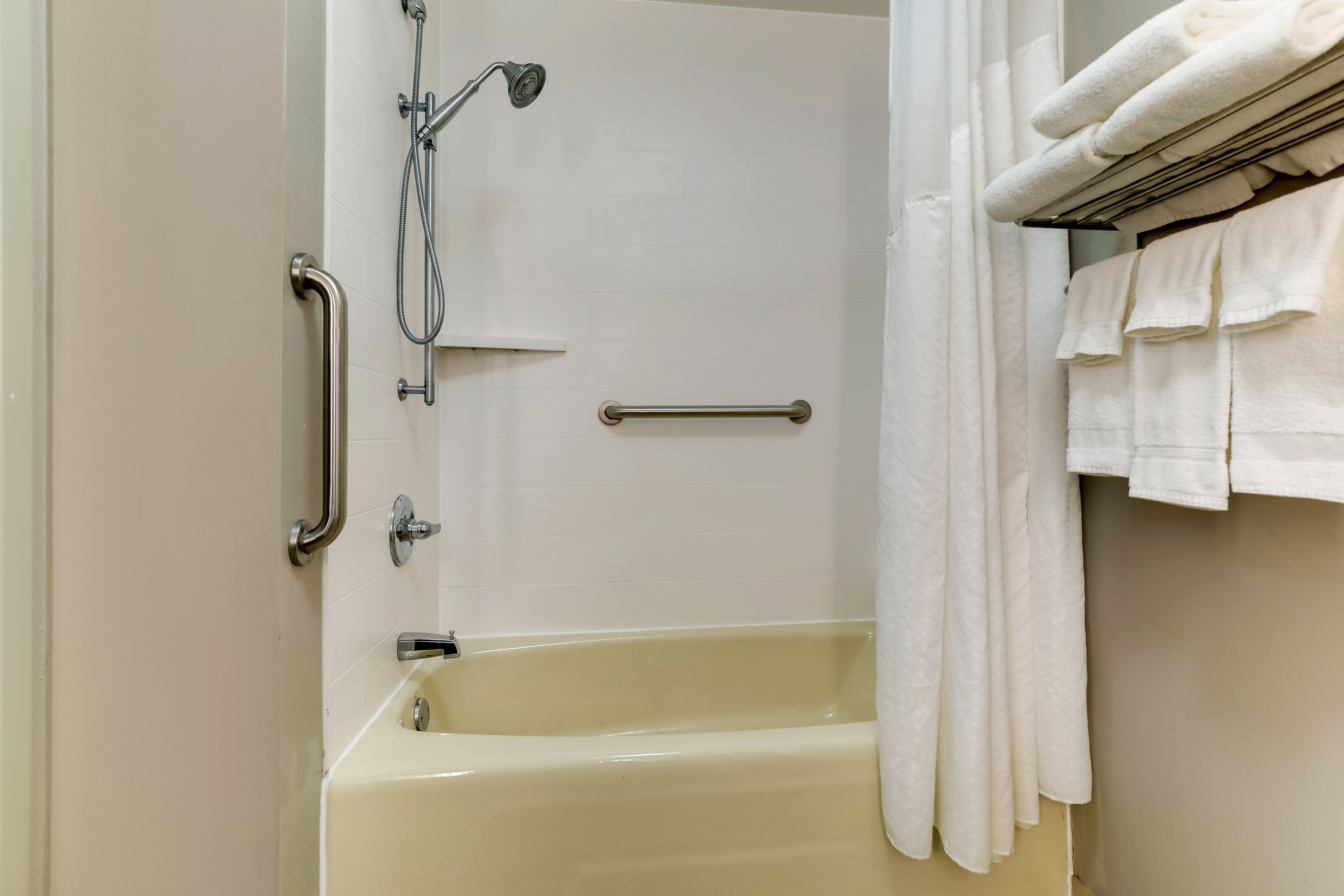 A bathroom with a bathtub, a shower with a handheld showerhead, and a towel rack with folded towels.