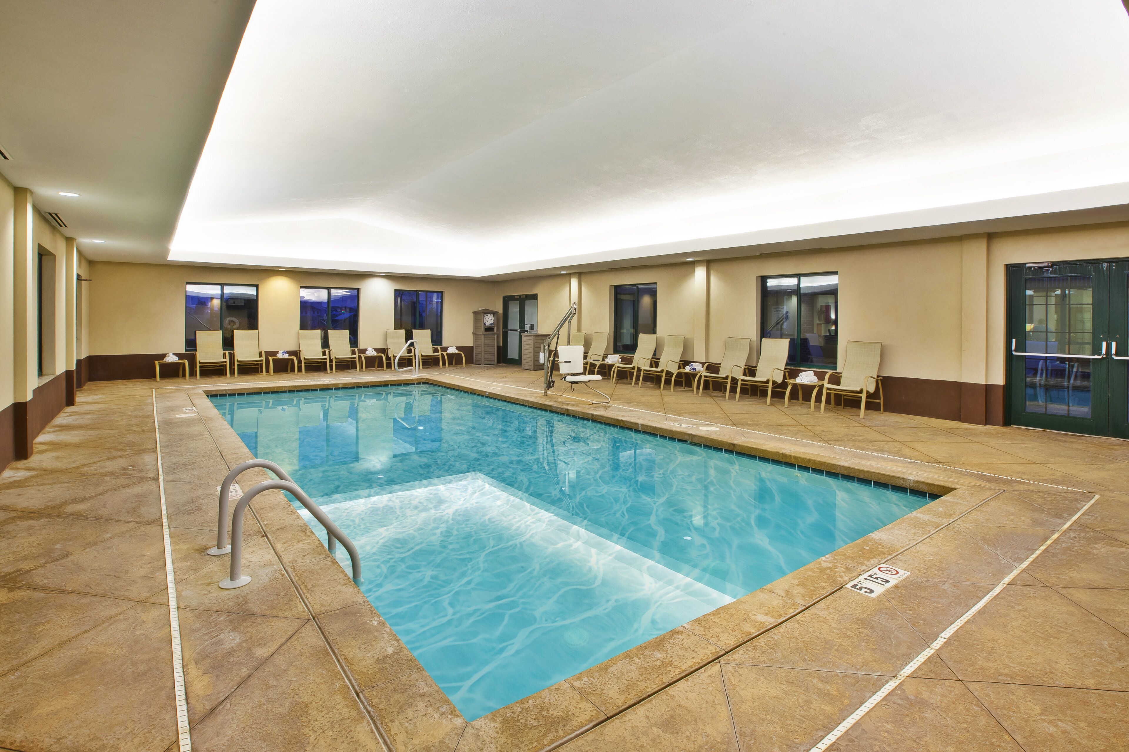 Una amplia piscina interior con múltiples sillas de descanso y una vista despejada del cielo a través de las ventanas.