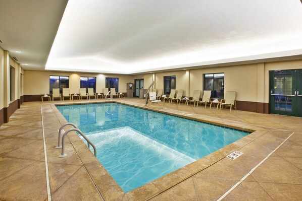 A large indoor swimming pool with multiple lounge chairs and a clear view of the sky through the windows.