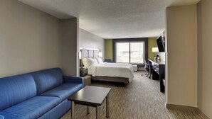 A hotel room with a blue sofa, a small table, a bed with a white comforter, a desk with a computer, and a TV. - Holiday Inn Express & Suites Montpelier by IHG (Montpelier)