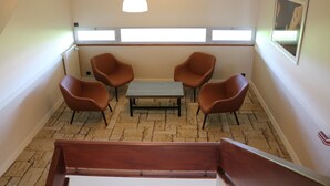 A room with a wooden bench, two brown chairs, a small table, and a window with blinds. - Hôtel de la Digue (Le Mont-Saint-Michel)
