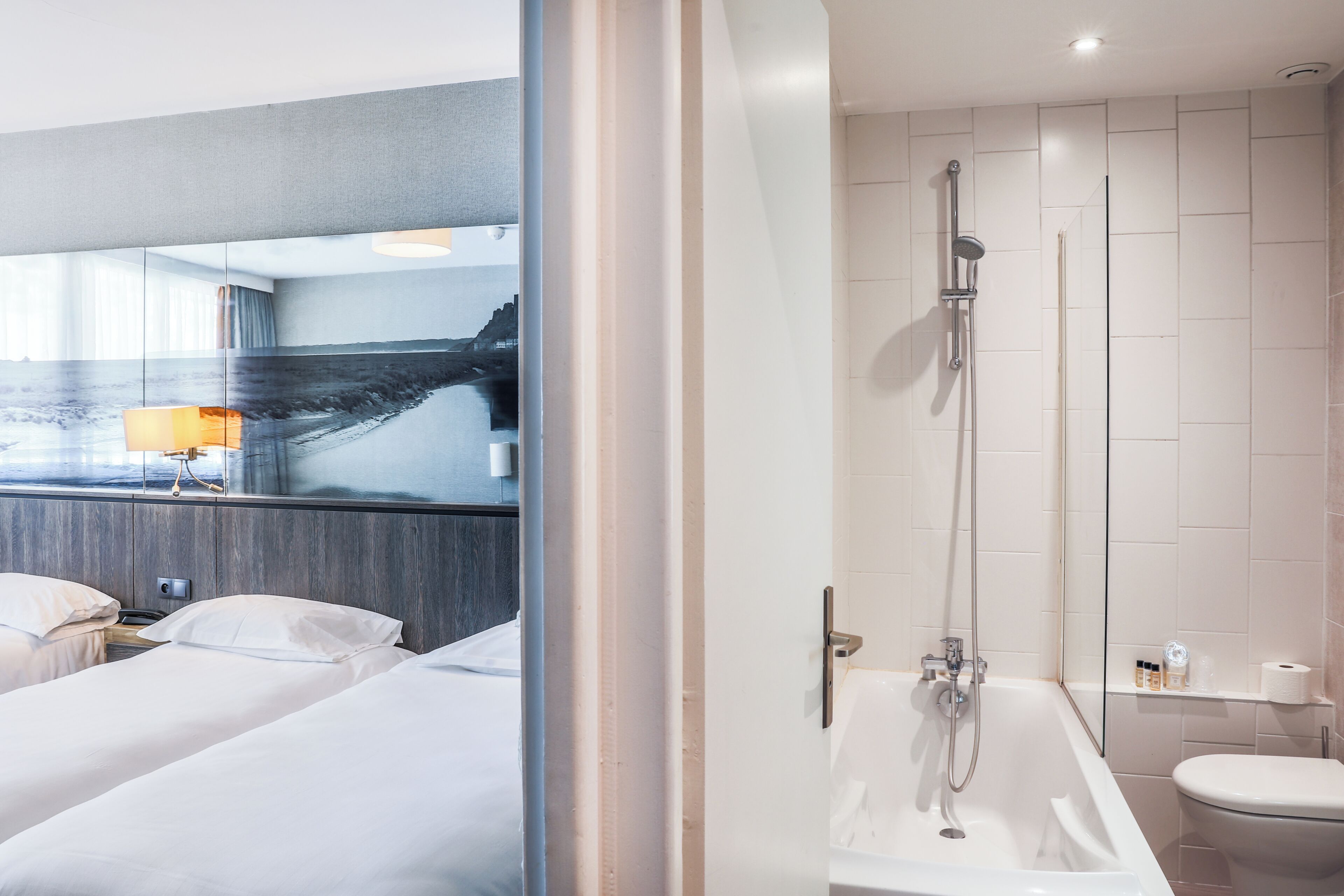 Una habitación de hotel con cama, baño con ducha y un espejo grande.