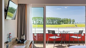 A hotel room with a balcony, a desk with a coffee maker, a TV, and a view of a green landscape. - Hôtel de la Digue (Le Mont-Saint-Michel)