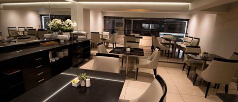 Un espace repas moderne avec une table centrale, entourée de chaises, et un coin cuisine avec des placards et des appareils électroménagers en arrière-plan.