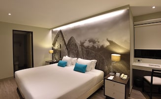 Una habitación de hotel con una cama grande, un escritorio con silla, un teléfono y una lámpara de pared.