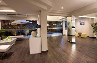 Un interior moderno con un separador de vidrio, un mostrador de recepción blanco y una zona de estar con cojines amarillos.