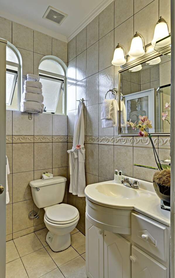 A bathroom with a toilet, sink, and mirror. There are towels hanging on the wall and a window above the toilet. - Casa Conde Apartamentos (San José)
