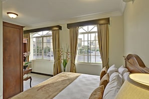 Habitación de hotel con una cama grande, un escritorio y vistas a la calle a través de amplios ventanales.