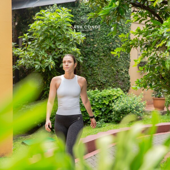 A woman walking in a garden area with greenery and a building in the background. - Casa Conde Apartamentos (San José)