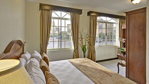 Ein Hotelzimmer mit einem großen Bett, einem Schreibtisch, einer Lampe und Blick auf die Straße durch die Fenster.