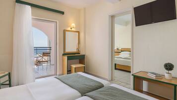 Ein Hotelzimmer mit zwei Betten, einem Schreibtisch, einem Sessel, einem Fernseher und einem Balkon mit Blick.