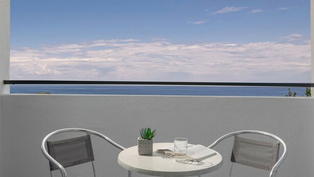 Un balcon avec une table ronde, deux chaises, une petite plante en pot et un verre d’eau.