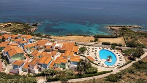 Vista aèria d'una estació turística a la costa amb viles, una piscina i aigües blaves i cristal·lines.