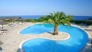 Une piscine avec un palmier au centre, entourée de chaises longues et de parasols.