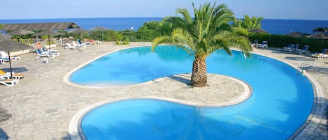A swimming pool with a palm tree in the center, surrounded by lounge chairs and umbrellas.