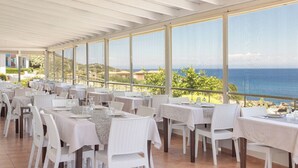 Un restaurant doté d’une terrasse, de tables et de chaises blanches, offrant une vue panoramique sur la mer.