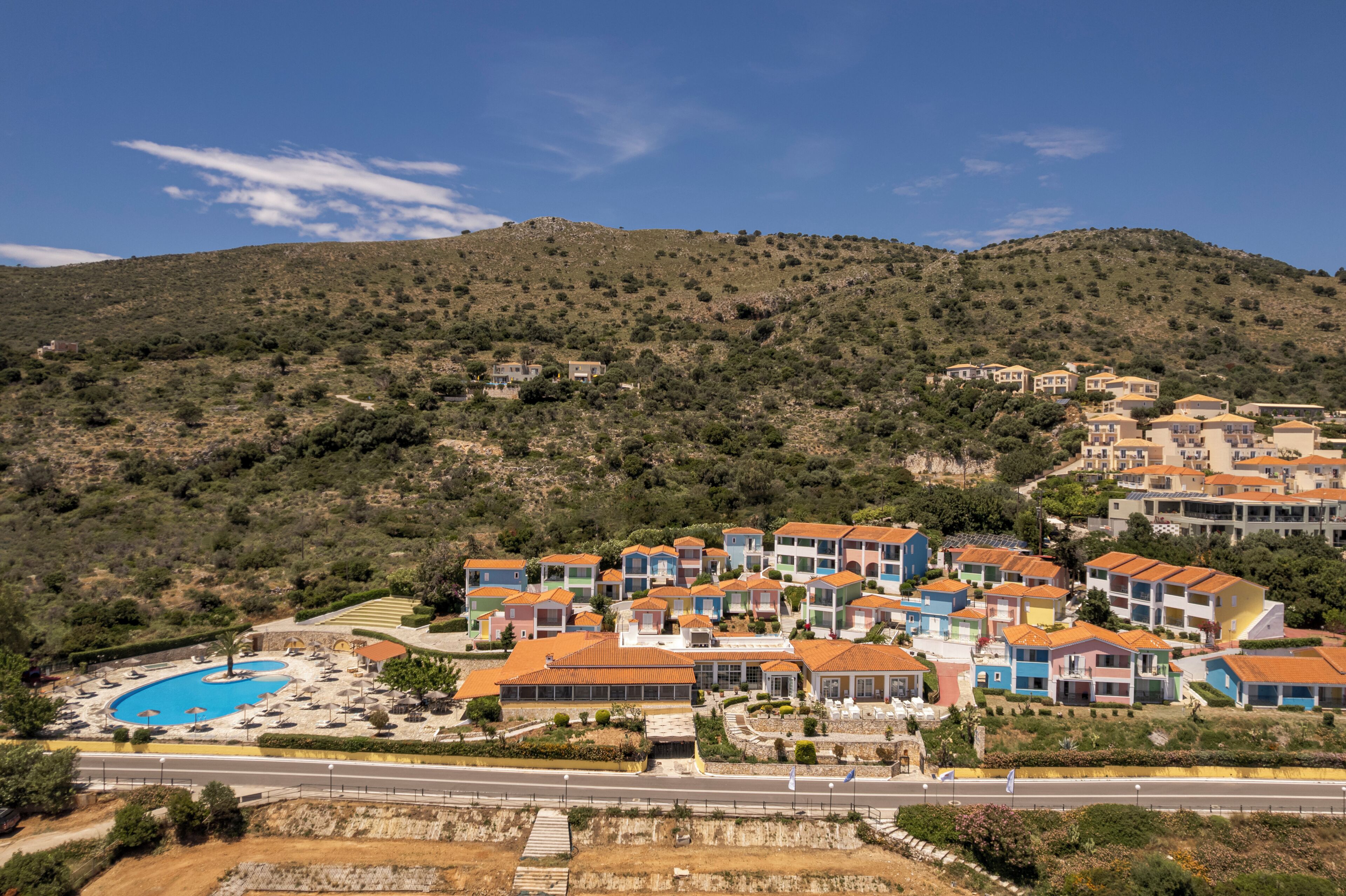 Um resort à beira-mar com edifícios coloridos, uma piscina e um cenário montanhoso.