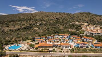 Um resort à beira-mar com edifícios coloridos, uma piscina e um cenário montanhoso.