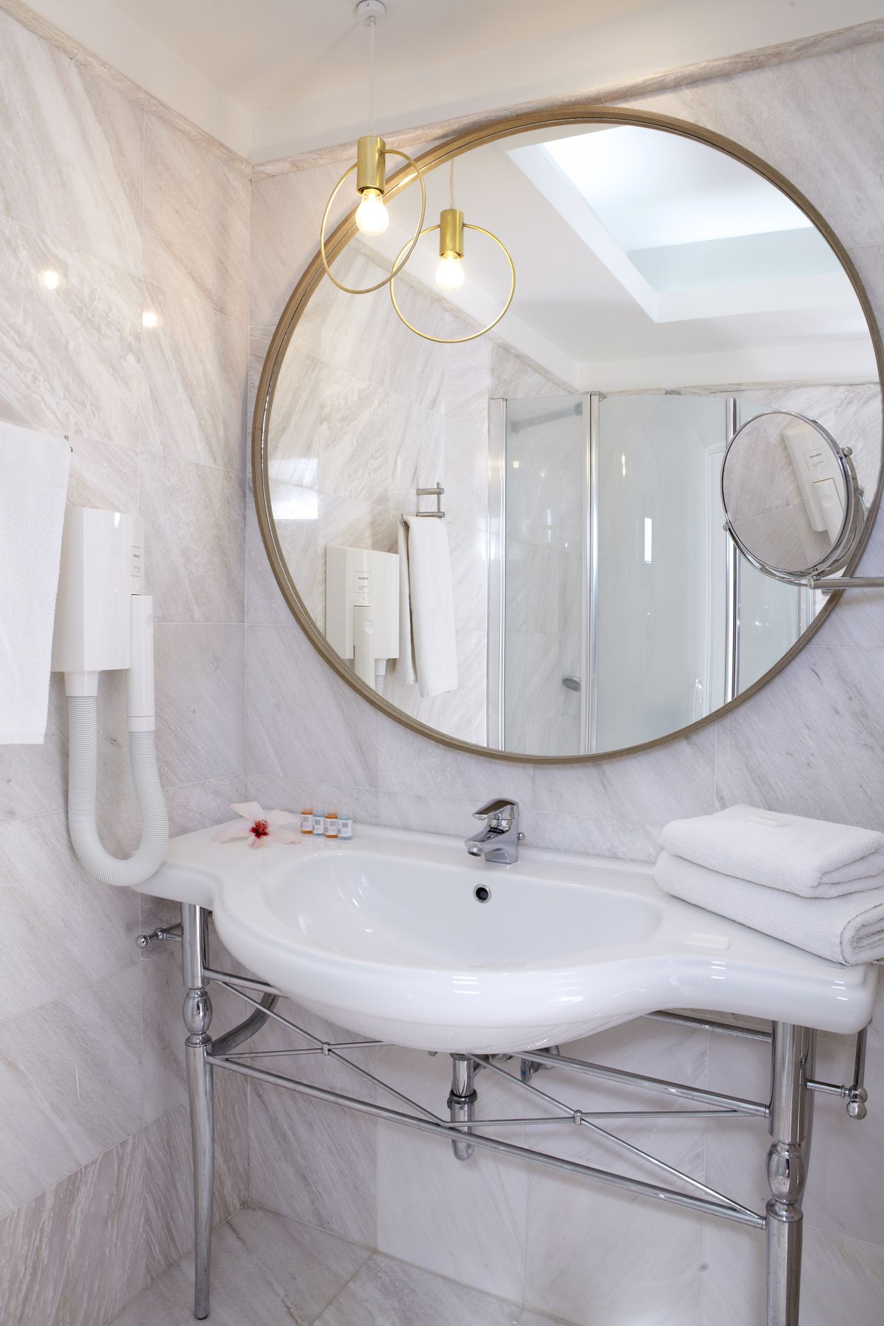 Un baño con lavamanos blanco, espejo redondo y cabina de ducha.