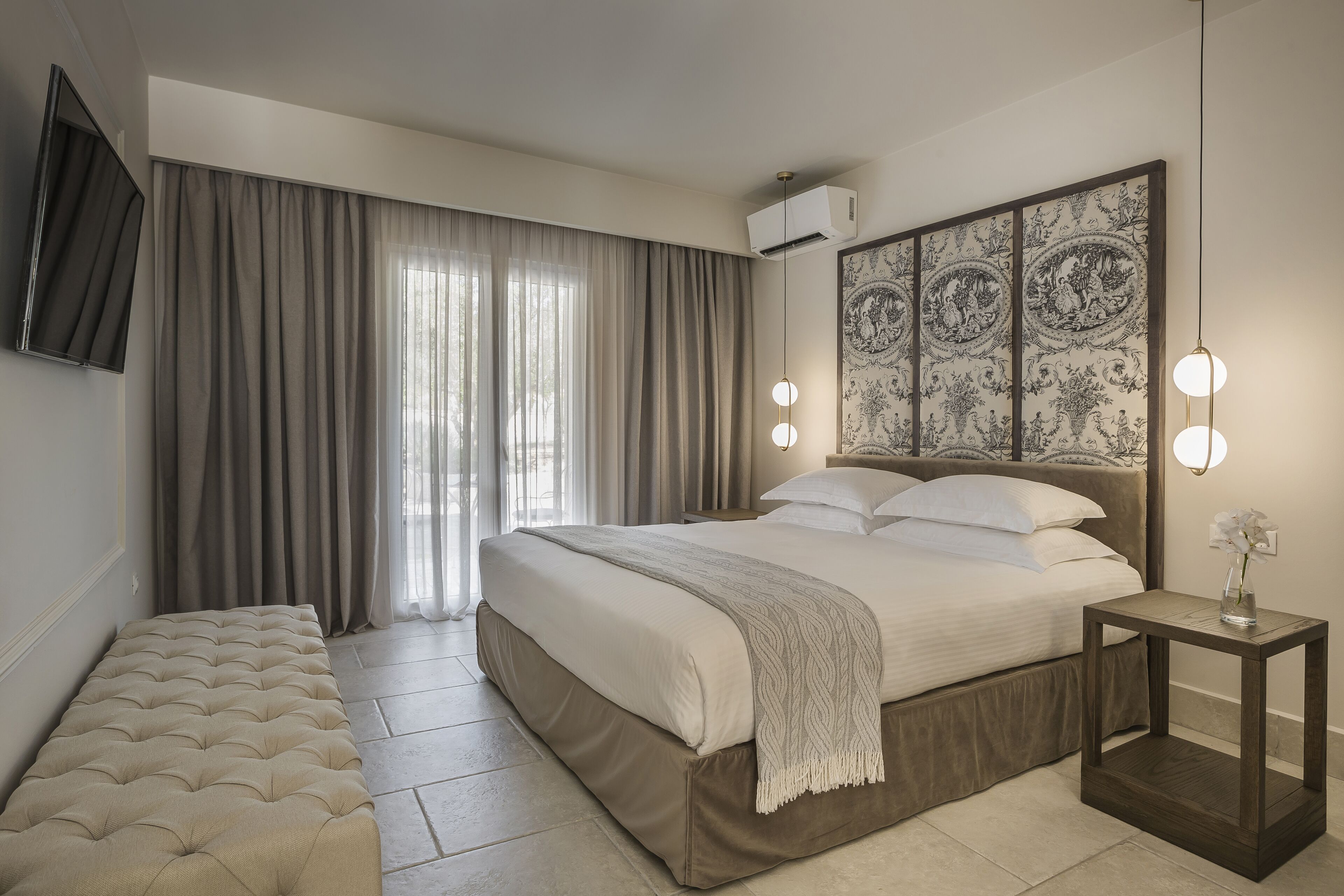 A modern bedroom with a large bed, a bench, a bedside table with a lamp, and a decorative wall piece.