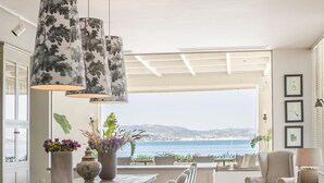 A spacious living area with a large table, multiple chairs, and a view of the sea. - Thalassa Boutique Hotel - Adults Only (Kefalonia)