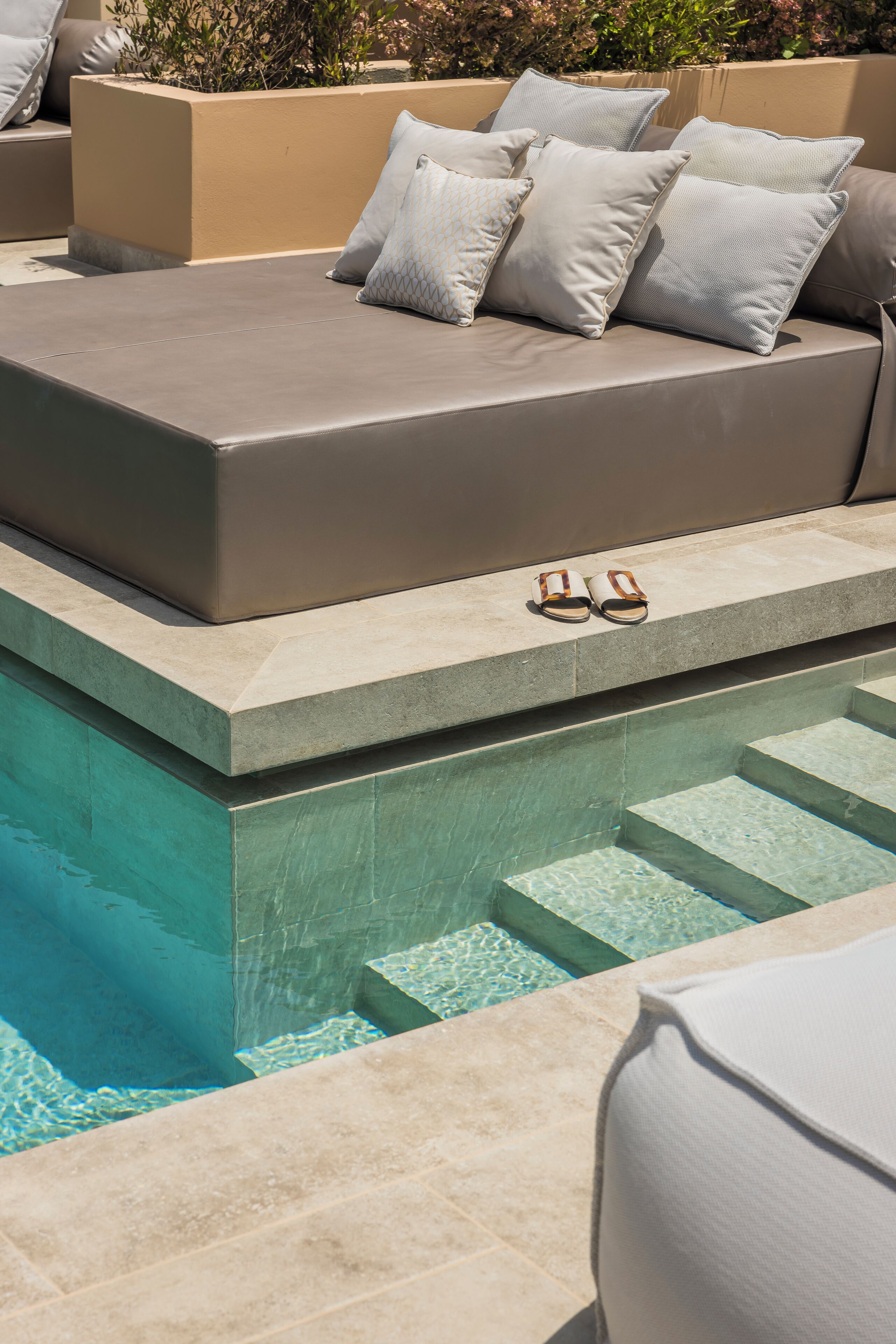 Zona de piscina con un espacio de descanso integrado y un par de sandalias al borde.