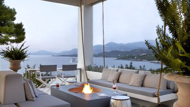 A modern outdoor seating area with a fire pit, sofas, and a view of a lake and mountains. - Thalassa Boutique Hotel - Adults Only (Kefalonia)