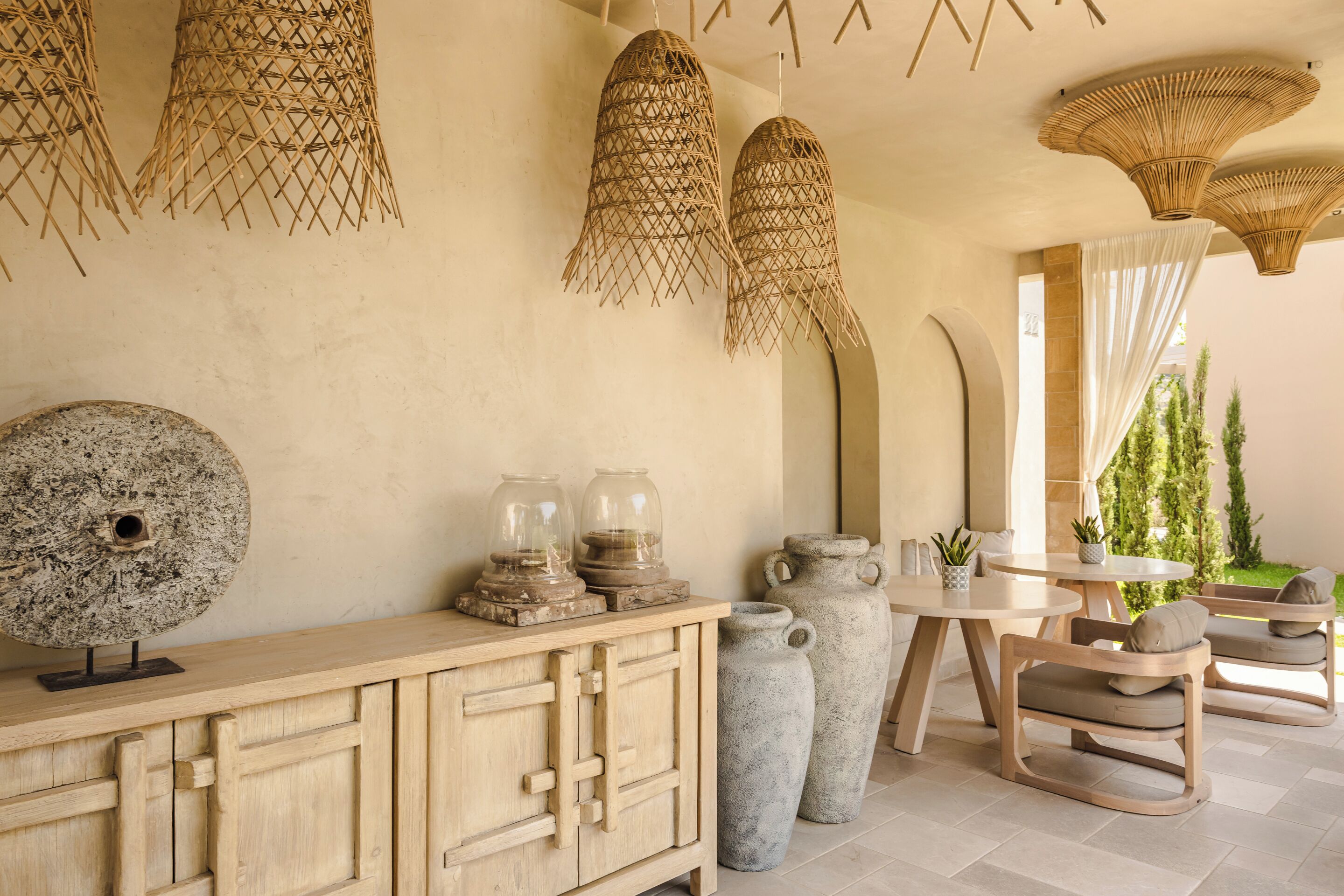 Una habitación con un armario de madera, dos jarrones grandes, lámparas de techo de mimbre y vistas al exterior con vegetación.