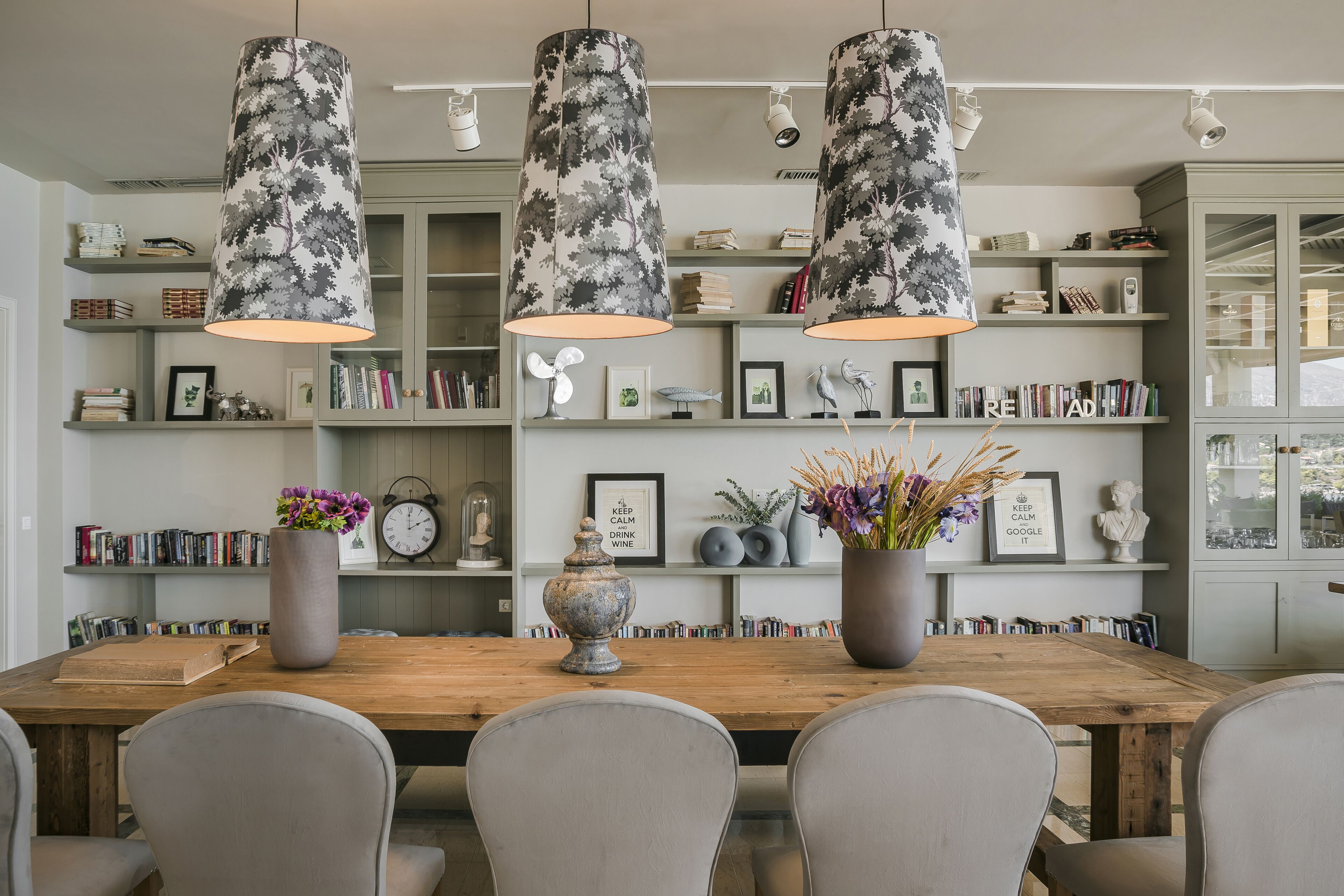 Een eetruimte met een houten tafel, grijze stoelen en drie hanglampen met bloemenmotieven.