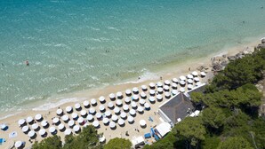 An aerial view of a beach with numerous round umbrellas and a building with a sloped roof. - Thalassa Boutique Hotel - Adults Only (Kefalonia)