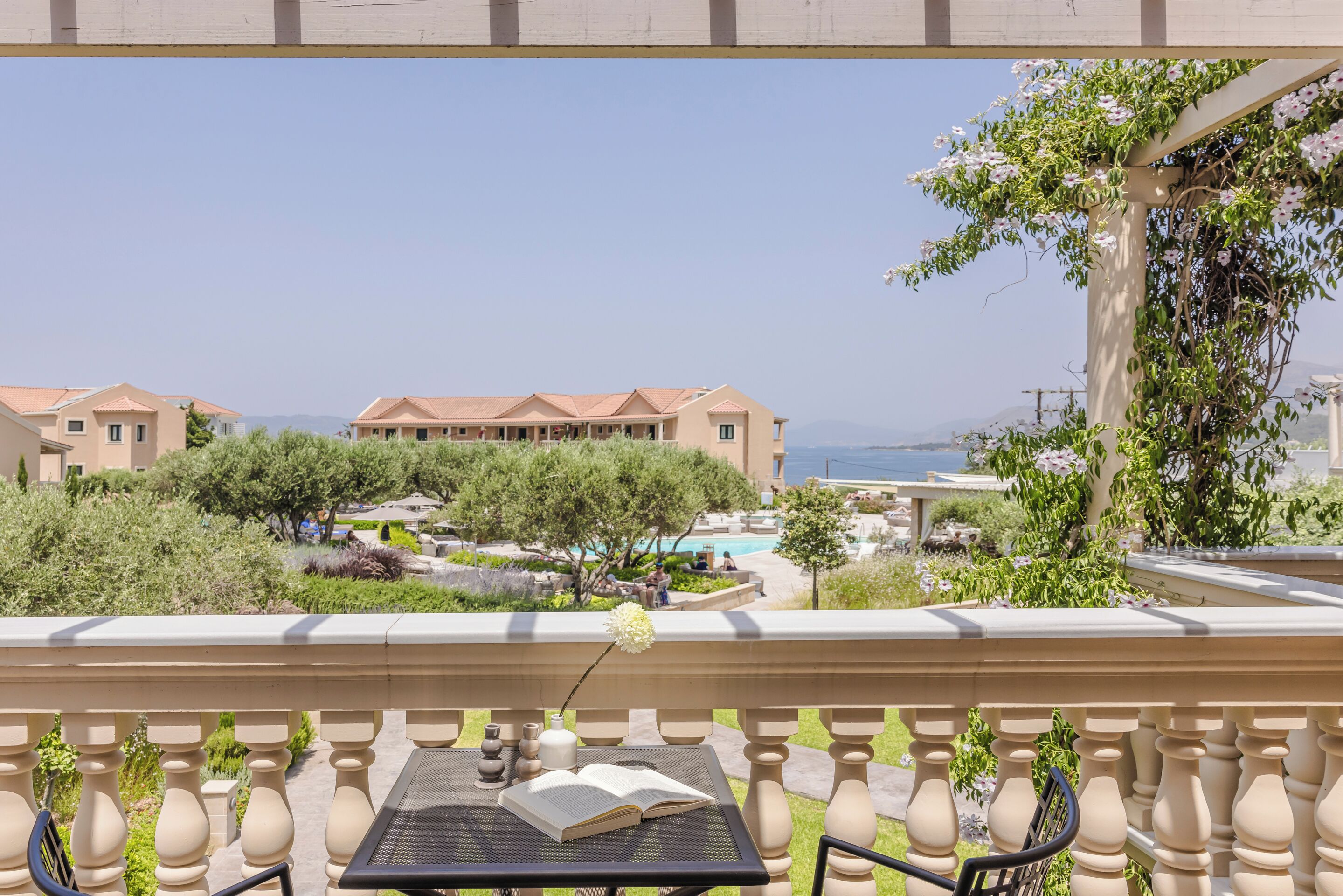 A balcony with a view of a pool, a building with a Mediterranean architectural style, and a clear sky.