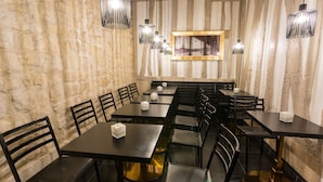 Un restaurante con mesas y sillas negras, una pared de piedra y lámparas colgantes.