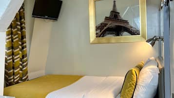 A hotel room with a bed, a desk, a chair, a television, a framed picture of the Eiffel Tower, and a window with curtains.