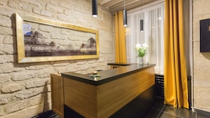Un mostrador de recepción con detalles de madera, un cuadro en la pared y una ventana con cortinas amarillas.