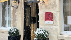 Entrada de un hotel, con un letrero que indica que es un hotel. Hay dos macetas negras con plantas cubiertas de nieve en la entrada.