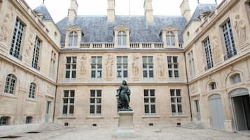 Ein Innenhof mit einer Statue in der Mitte, umgeben von einem Gebäude mit klassischer Architektur und zahlreichen Fenstern.