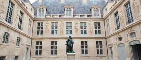 A courtyard with a statue in the center, surrounded by a building with classical architecture and multiple windows.