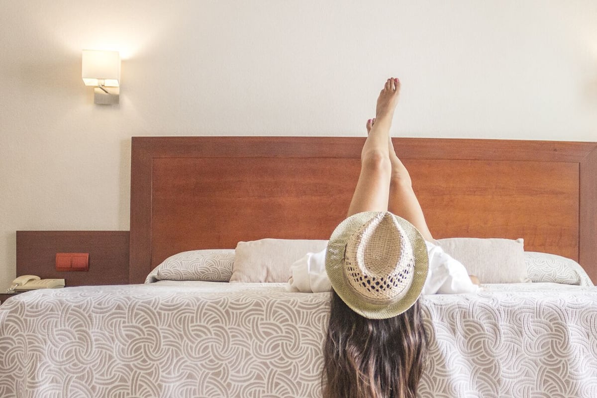 Una cama con cabecera de madera, ropa de cama blanca estampada y dos lámparas de noche.