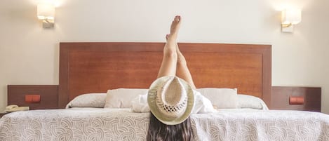 Una cama con cabecera de madera, ropa de cama blanca estampada y dos lámparas de noche.