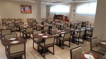 Un salón de conferencias con mesas y sillas, un cuadro en la pared y una ventana con persianas.