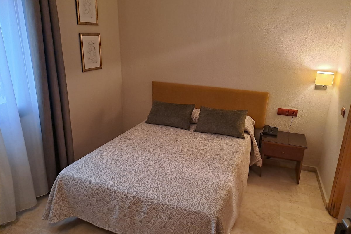 Una cama bien hecha con una colcha estampada, un cabecero de madera y una mesita de noche con una lámpara.