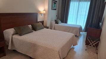 A hotel room with two beds, a nightstand, a lamp, a chair, and a window with curtains.