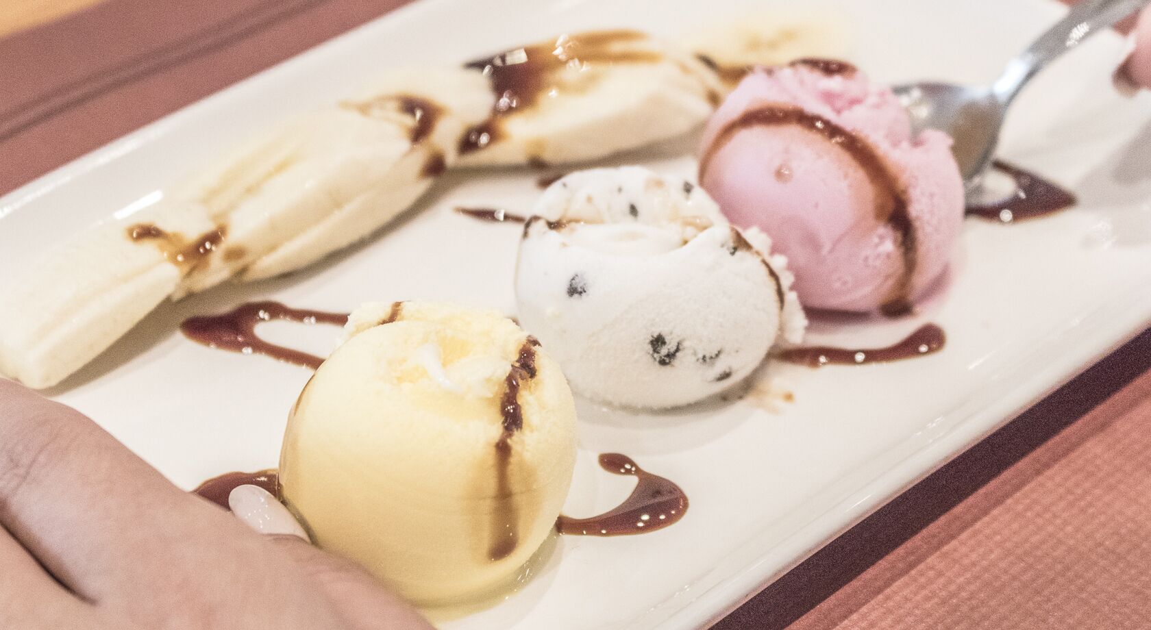 A dessert plate with three scoops of ice cream and chocolate sauce.