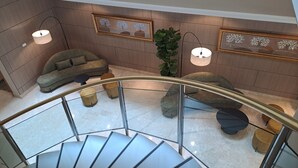 Un intérieur moderne avec un escalier en colimaçon, un canapé gris et une plante en pot.