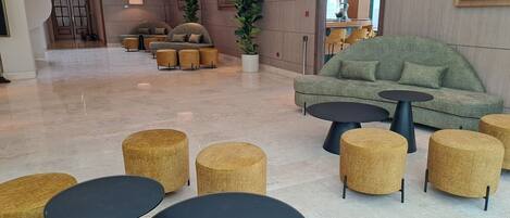 A modern lobby with a green sofa, round tables, and a staircase.