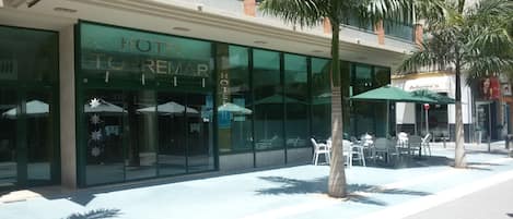 Un hotel con fachada de vidrio, zona de estar al aire libre y palmeras.