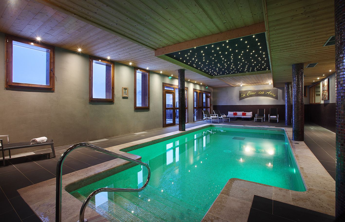 En indendørs swimmingpool med krystalklart vand, gelænder af glas og et stjernebelyst loft.