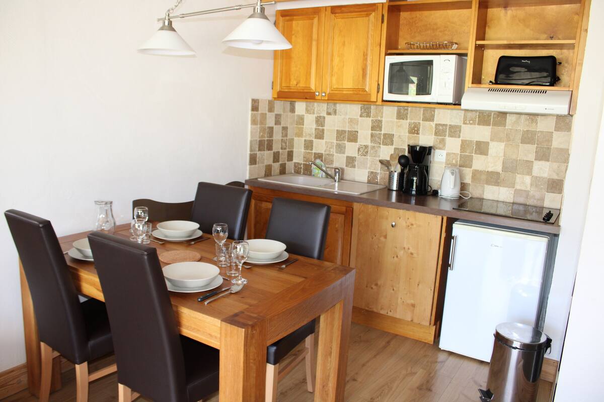 A compact kitchen with wooden cabinets, a microwave, a coffee maker, and a small refrigerator.
