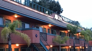A multi-story hotel with a red facade, balconies, and palm trees.