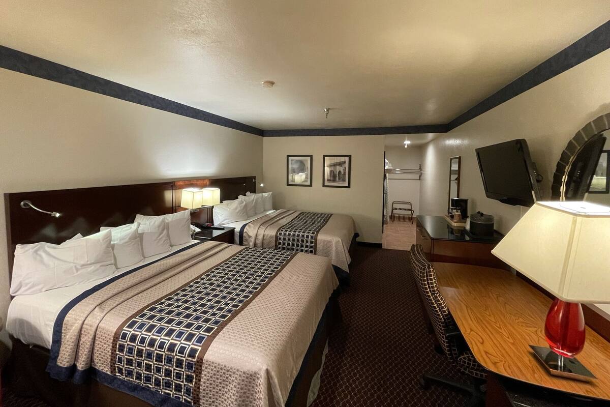 A hotel room with two beds, a desk with a lamp, a TV, and a bathroom visible in the background.